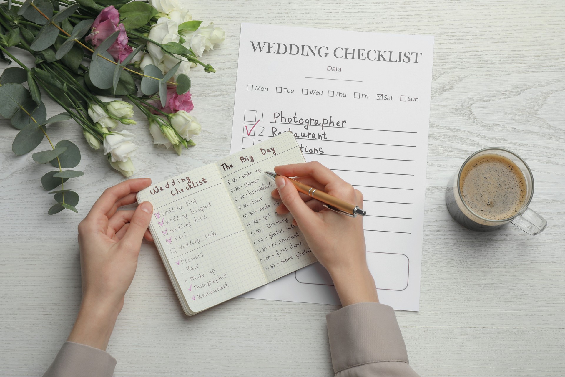Woman writing in Wedding Planner at white wooden table, top view